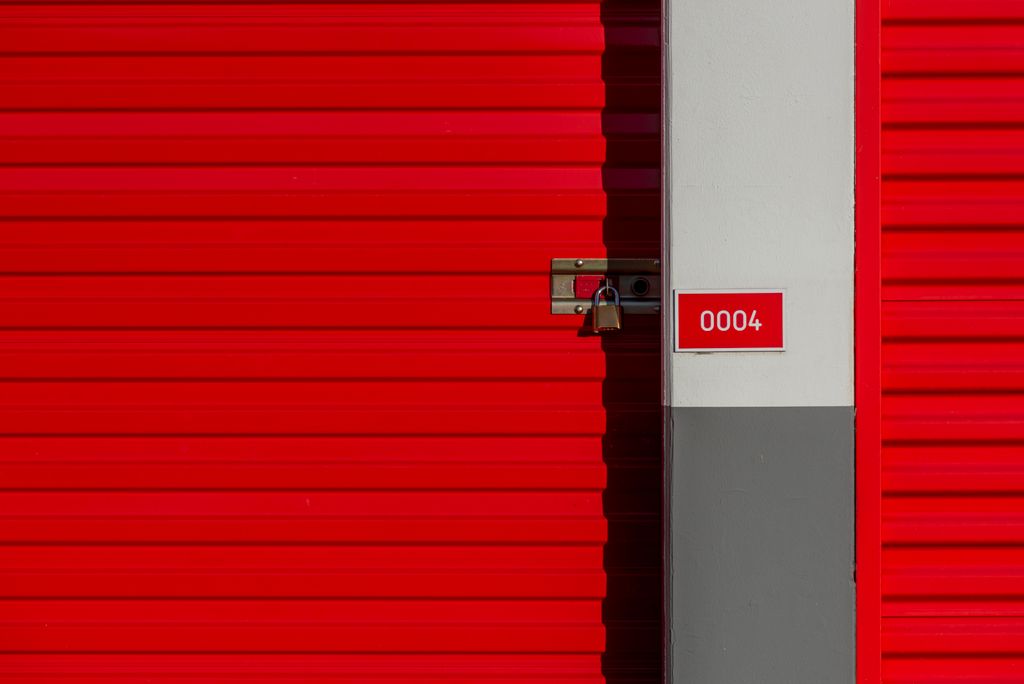 Red metal storage unit door with padlock and number 0004 sign on white panel.